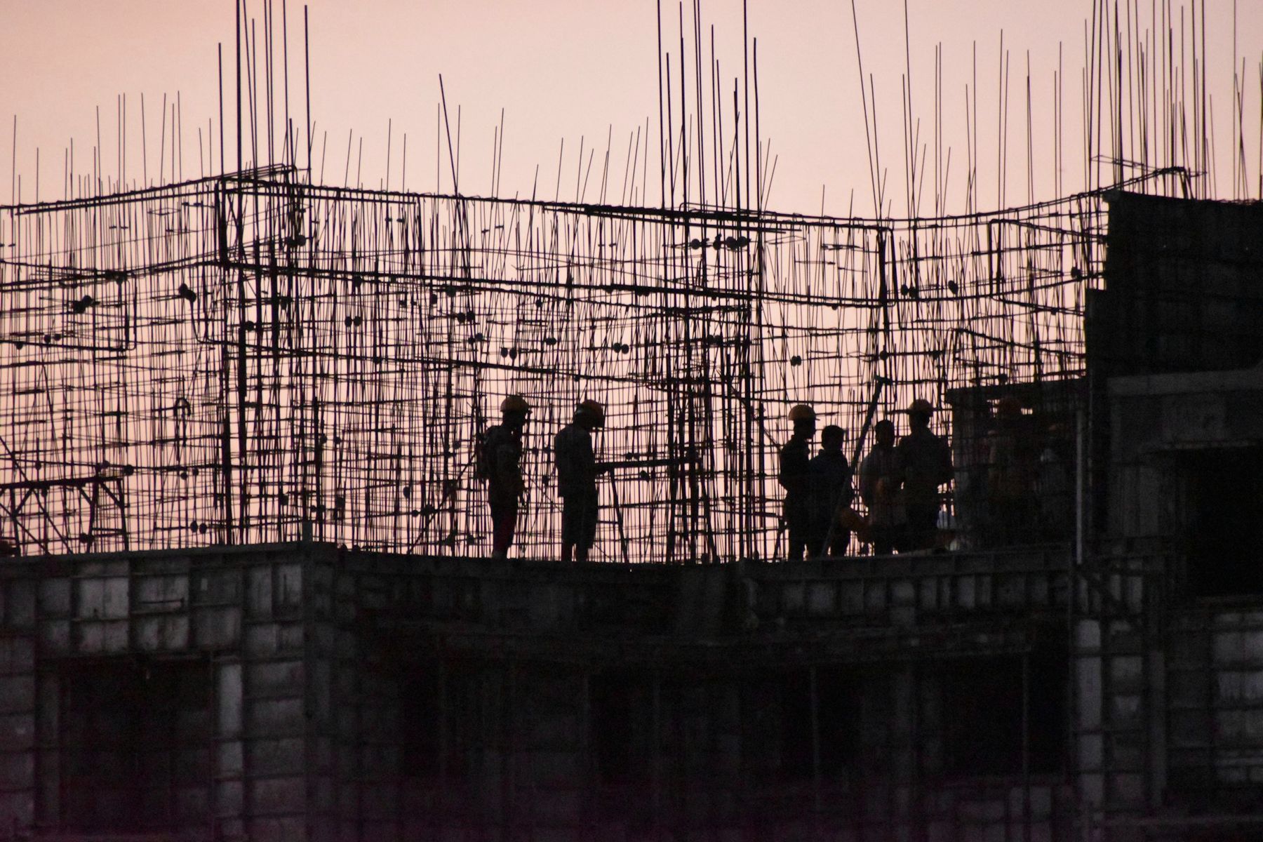 A site crew silhouetted against a dusk sky, working among the rebar of a rising concrete frame