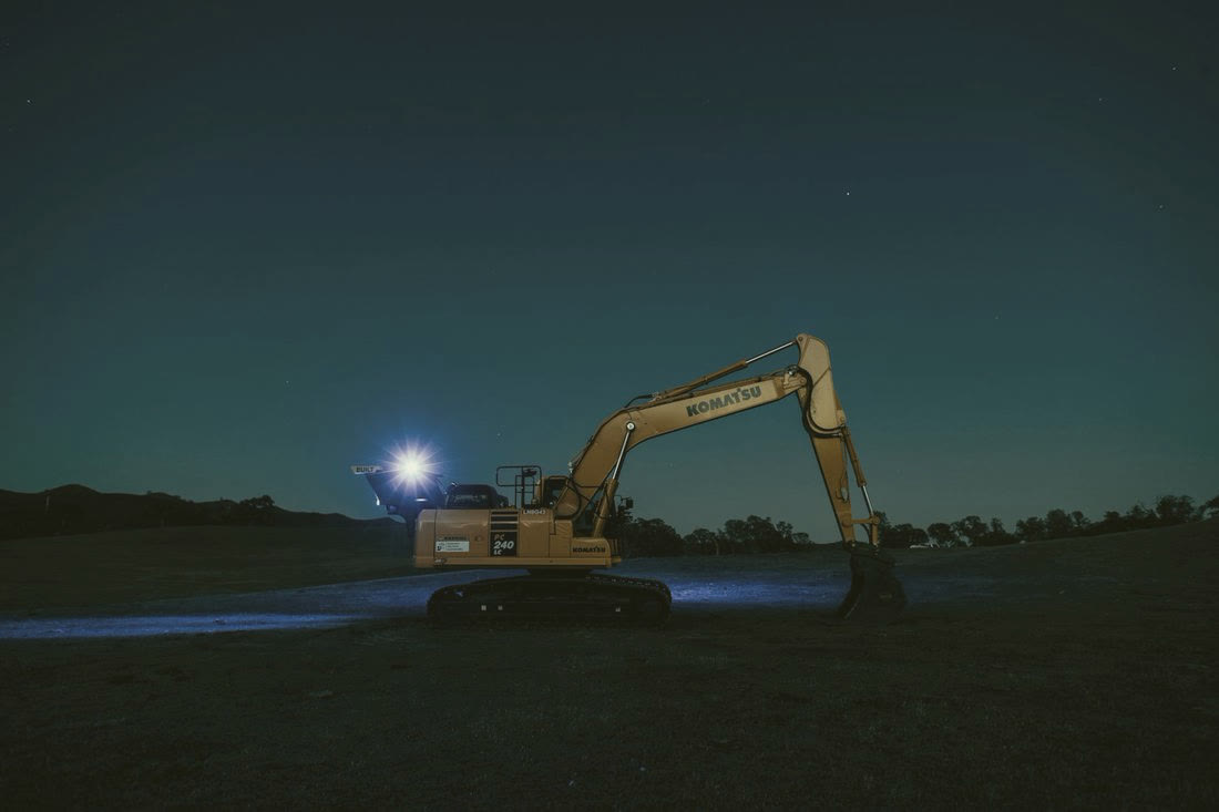 An excavator parked on open ground at night under a work light